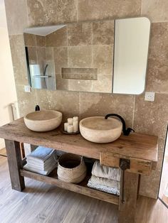 a bathroom with two sinks and mirrors on the wall next to a wooden shelf filled with towels