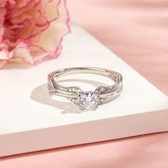 a diamond ring sitting on top of a white surface next to a pink peonie flower