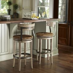 two wooden stools sitting in front of a kitchen counter with plates and glasses on it