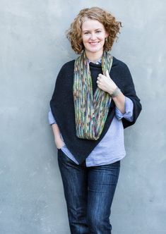 a woman standing in front of a gray wall wearing a multicolored knit scarf