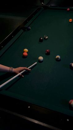 a person holding a pool stick in front of a pool table with balls on it