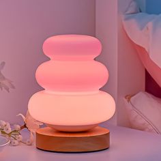 a pink lamp sitting on top of a table next to a white vase and flower