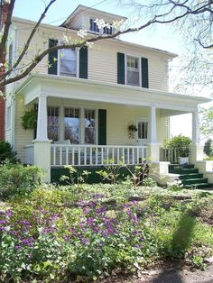 a white house with green shutters and flowers in the front yard