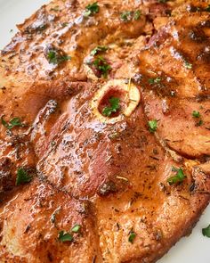 a piece of meat on a white plate with parsley sprinkled around it