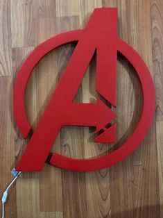 the avengers logo cut out from red paper on a wooden floor with an ipod plugged in