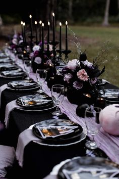 a long table is set with black and white plates, silverware, and purple flowers