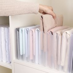 a person holding a bag in front of a white book shelf filled with folded clothes