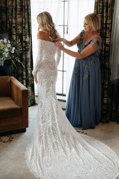 two women standing next to each other in front of a window wearing long white dresses