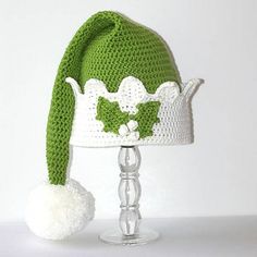 a crocheted green and white hat on top of a glass stand with a pom - pom