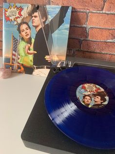 a blue record player sitting on top of a table next to a brick wall and an album