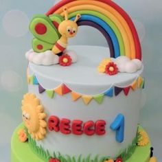 a birthday cake decorated with a rainbow, bee and flower decoration on the top tier