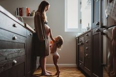 a woman standing next to a baby in a kitchen