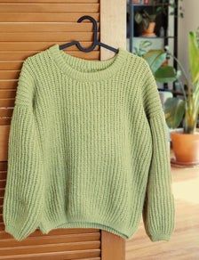 a green sweater hanging on a wooden door