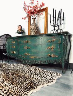 a green dresser sitting next to a mirror on top of a wooden floor covered in animal print rugs