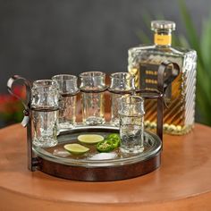 a tray that has glasses on it with some limes and a bottle in the background