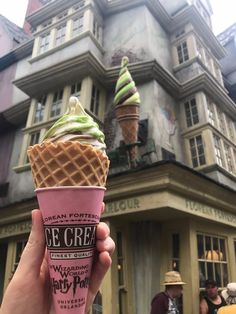 a hand holding an ice cream cone in front of a building