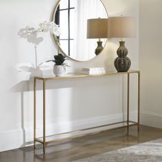 a gold console table with a round mirror on the wall above it and a lamp next to it