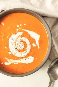 a bowl filled with carrot soup on top of a white cloth next to two spoons