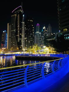 the city skyline is lit up at night with bright blue lights and reflections on the water