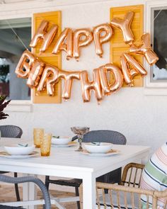 an outdoor birthday party with gold balloons and plates on the table, along with flowers