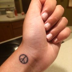 a woman's wrist with a small peace sign tattoo on the left side of her arm