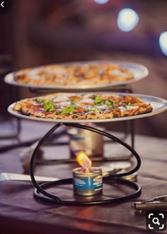 three pizzas on metal trays sitting on top of a table