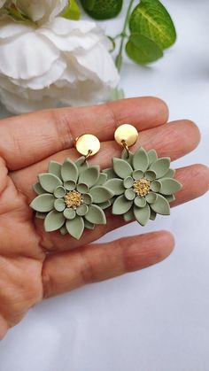 a pair of green flower earrings sitting on top of a hand