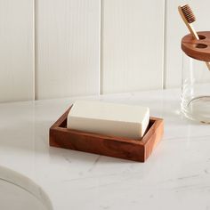 a toothbrush and soap in a wooden holder on a marble counter top next to a glass