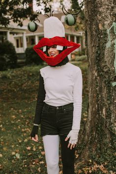 a woman in white shirt and black pants standing next to tree with red lips on it