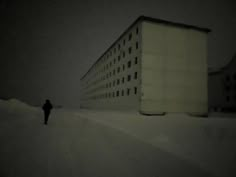 a person walking in the snow next to a tall building on a snowy day with no one around