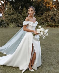 a woman in a white wedding dress holding a bouquet and posing for the camera with her long veil draped over her shoulder