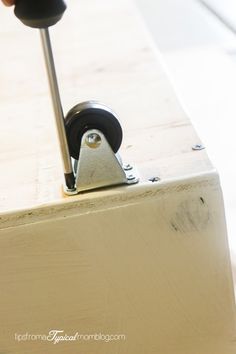 a hand holding a piece of wood with a tool on it's end and wheels attached to the board