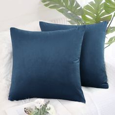 two blue pillows sitting on top of a white bed next to a potted plant