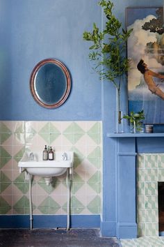 a bathroom with blue walls, green and white tiles and a painting on the wall