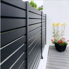 a large black fence next to a planter with yellow flowers on the side of it