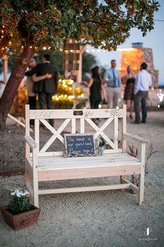 a wooden bench sitting under a tree next to a chalkboard on top of it