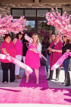 a group of women holding pink ribbon and scissors in front of a building with flowers on it