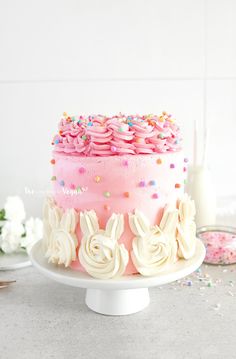 a pink cake with white frosting and sprinkles on top is sitting on a plate