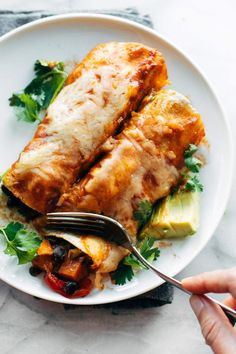 someone is holding a fork and knife over a plate of enchiladas with avocado