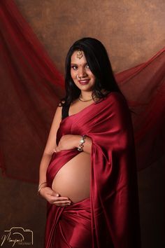 a pregnant woman in a red sari poses for a photo with her belly exposed