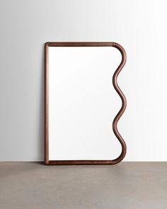 a mirror sitting on top of a cement floor next to a white wall with a wooden frame