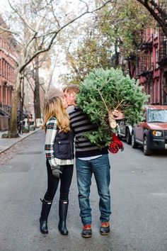 a man and woman are standing in the street with a christmas tree on their shoulders