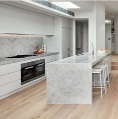 a kitchen with white cabinets and marble counter tops, along with an island in the middle