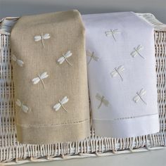 three folded towels in a wicker basket on a shelf with white linens and dragonflies