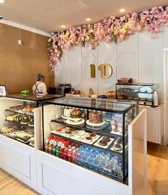 a display case filled with lots of cakes and desserts next to a wall covered in flowers