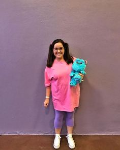 a girl standing in front of a purple wall holding a blue stuffed animal and smiling at the camera