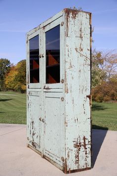 an old white cabinet sitting on top of a cement ground next to a green field