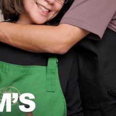 two people hugging each other while wearing green aprons and black shirts with the words mom's written on them