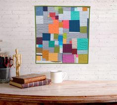 a coffee cup sitting on top of a wooden table next to a wall hanging quilt