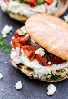 an open faced sandwich with tomatoes, cheese and herbs on it sitting on a black surface